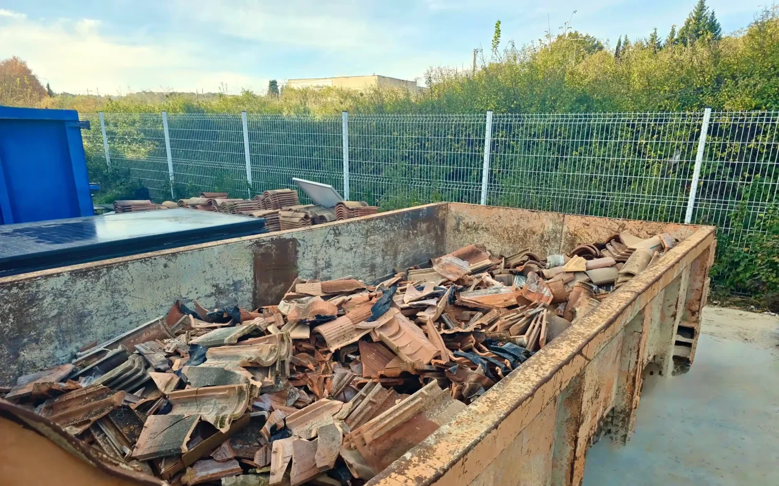 Benne de chantier remplie de tuiles de toiture déposées lors d’une installation de panneaux solaires C.O.A, gestion des déchets et recyclage.