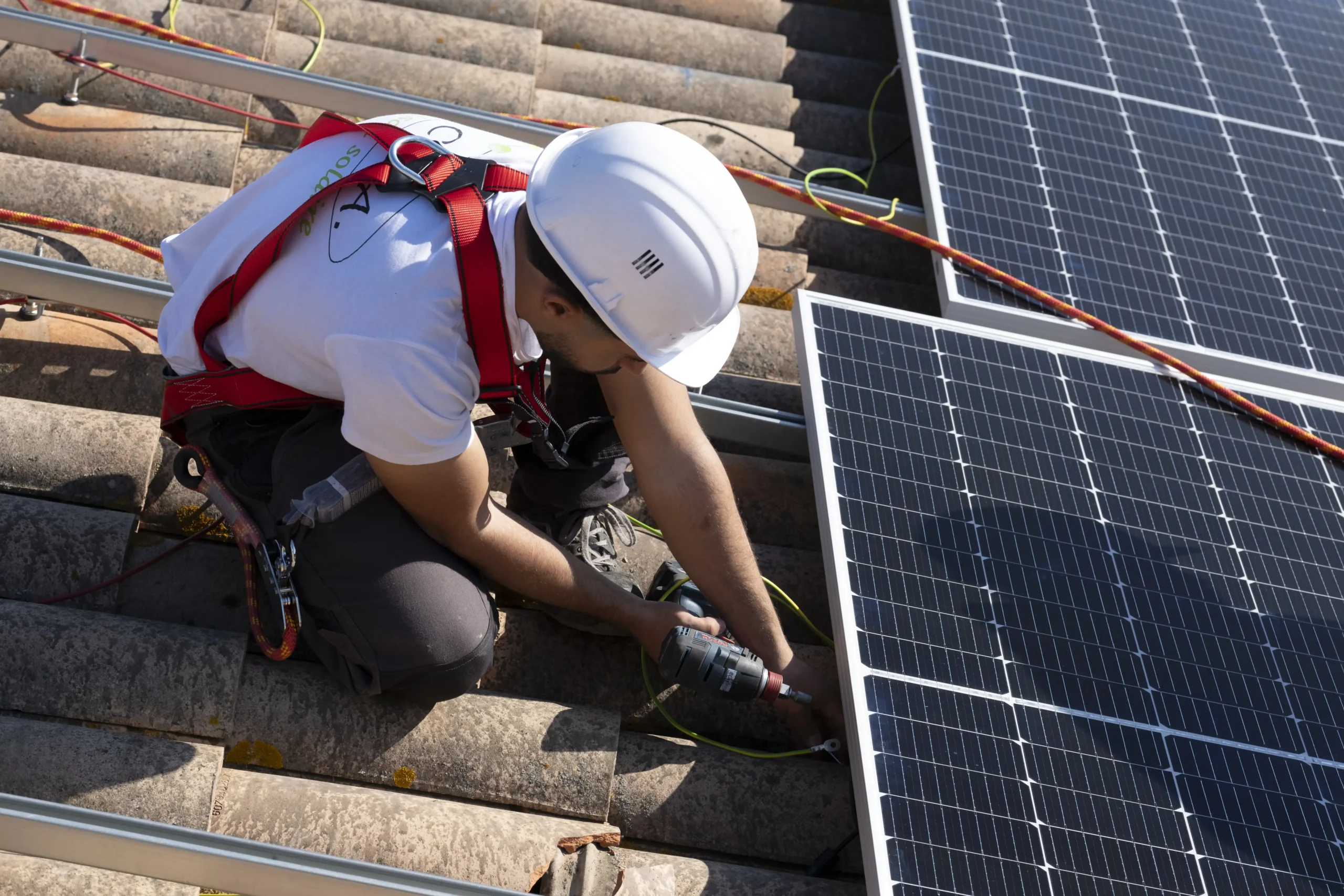 Artisan solaire C.O.A raccordant un panneau photovoltaïque sur toiture en tuiles, câblage et mise à la terre de l’installation solaire.